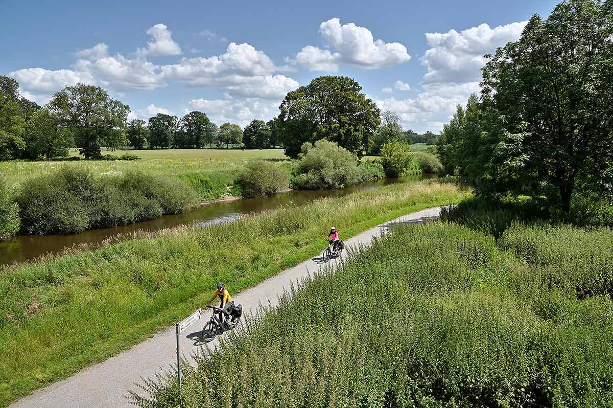 Radfahrer auf einem Radweg der parallet zu einem Fluß verläuft in einer typisch münsterländischen Landschaft